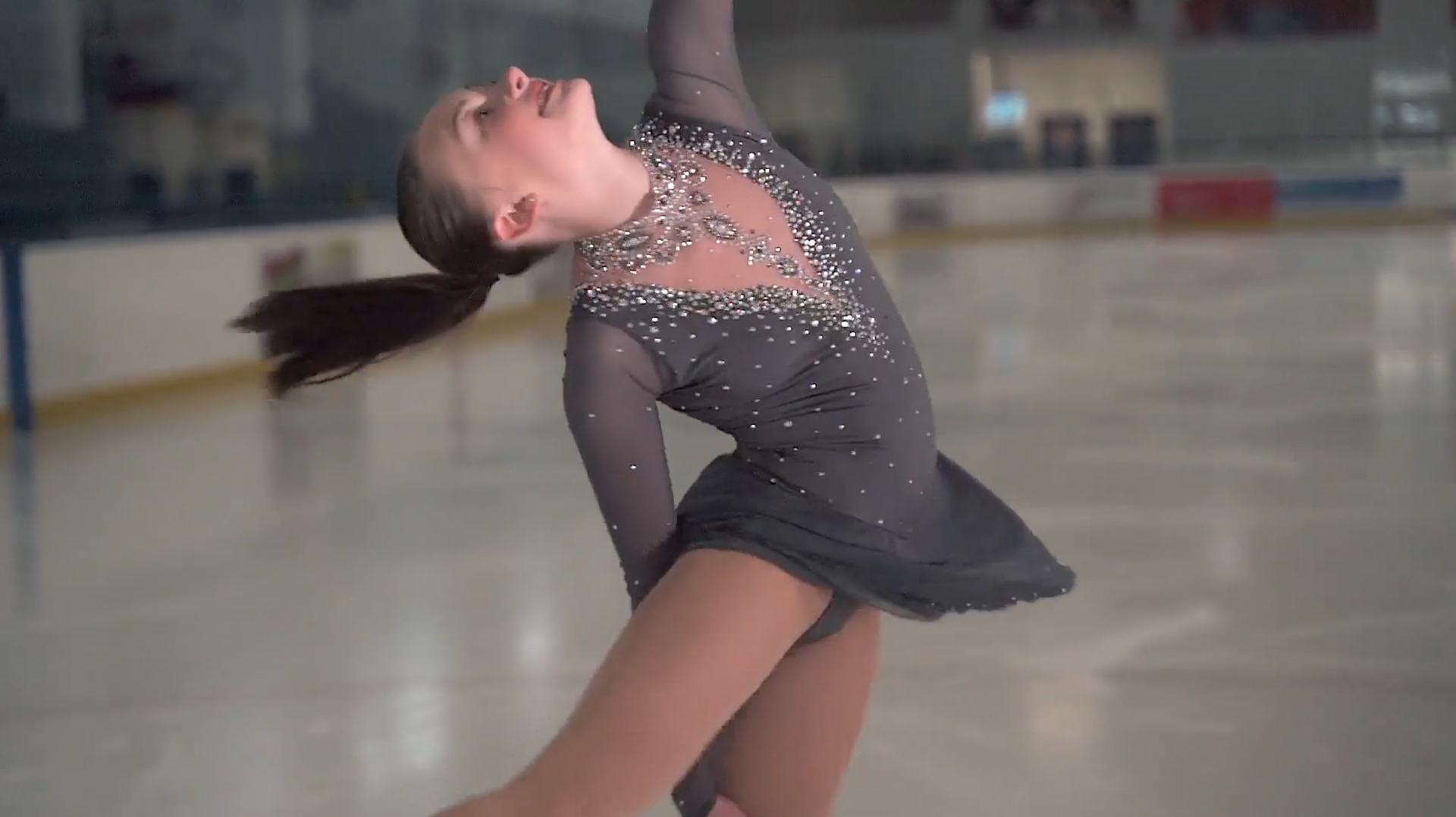 A woman in a gray dress is ice skating on a rink.