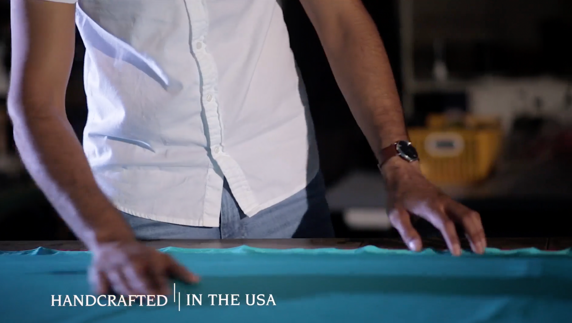 A man in a white shirt is cutting a piece of blue fabric.