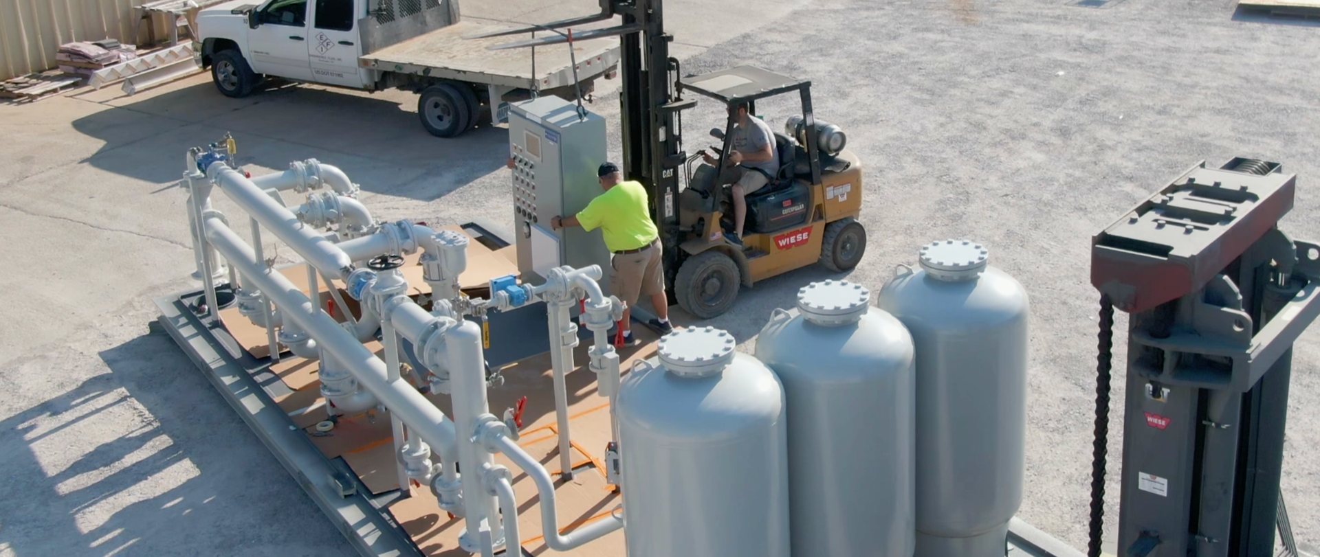 A man is driving a forklift in a parking lot next to a truck.