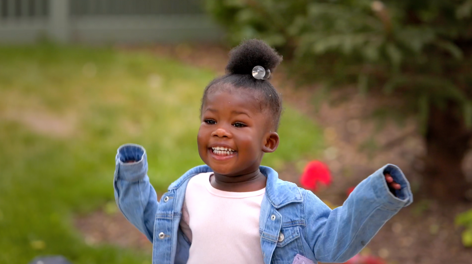 A little girl is standing in the grass with her arms in the air.