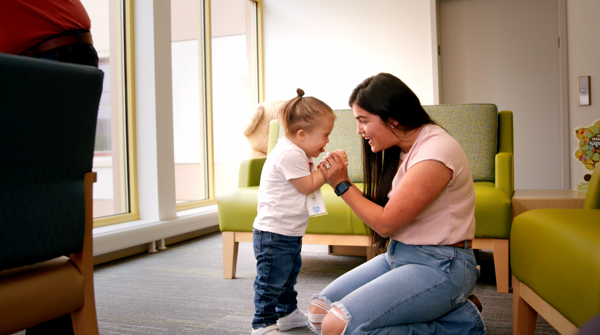 A woman is kneeling down next to a little girl in a waiting room.