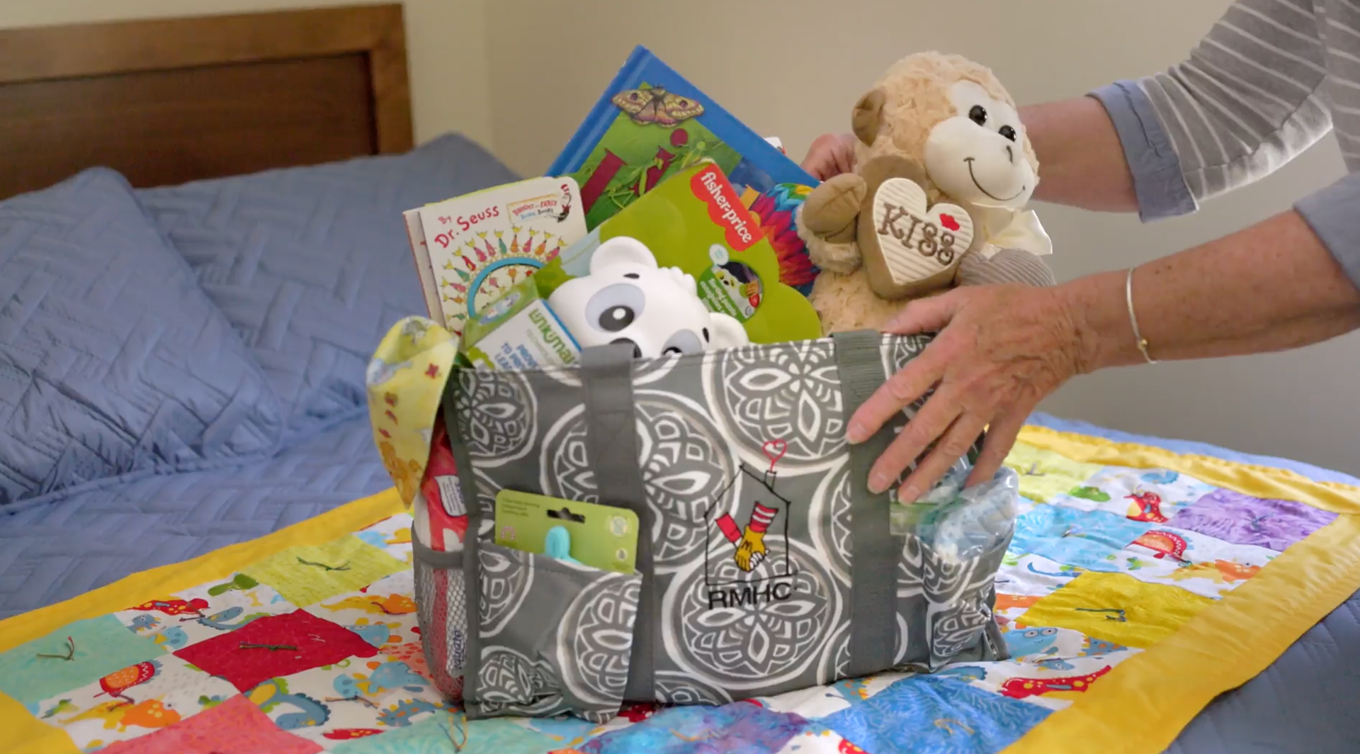 A person is holding a basket of toys on a bed.