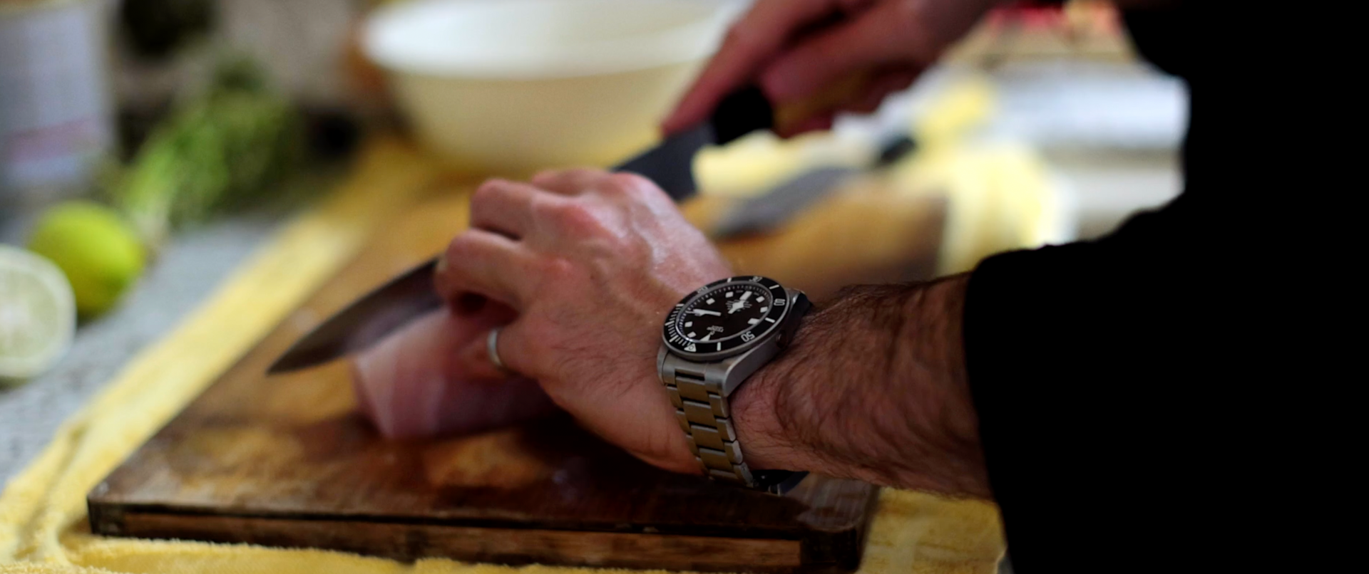 A man wearing a watch is cutting food on a cutting board