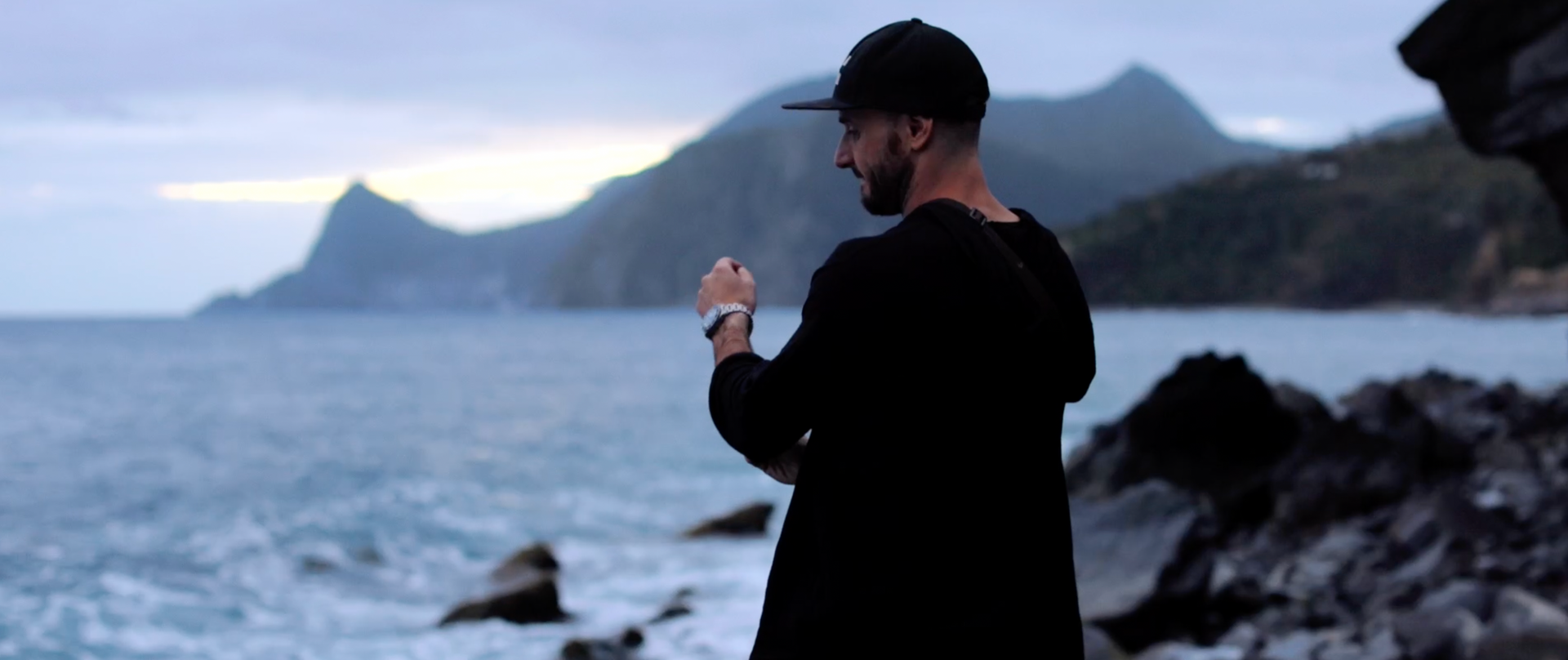 A man is standing on a rocky beach looking at the ocean.