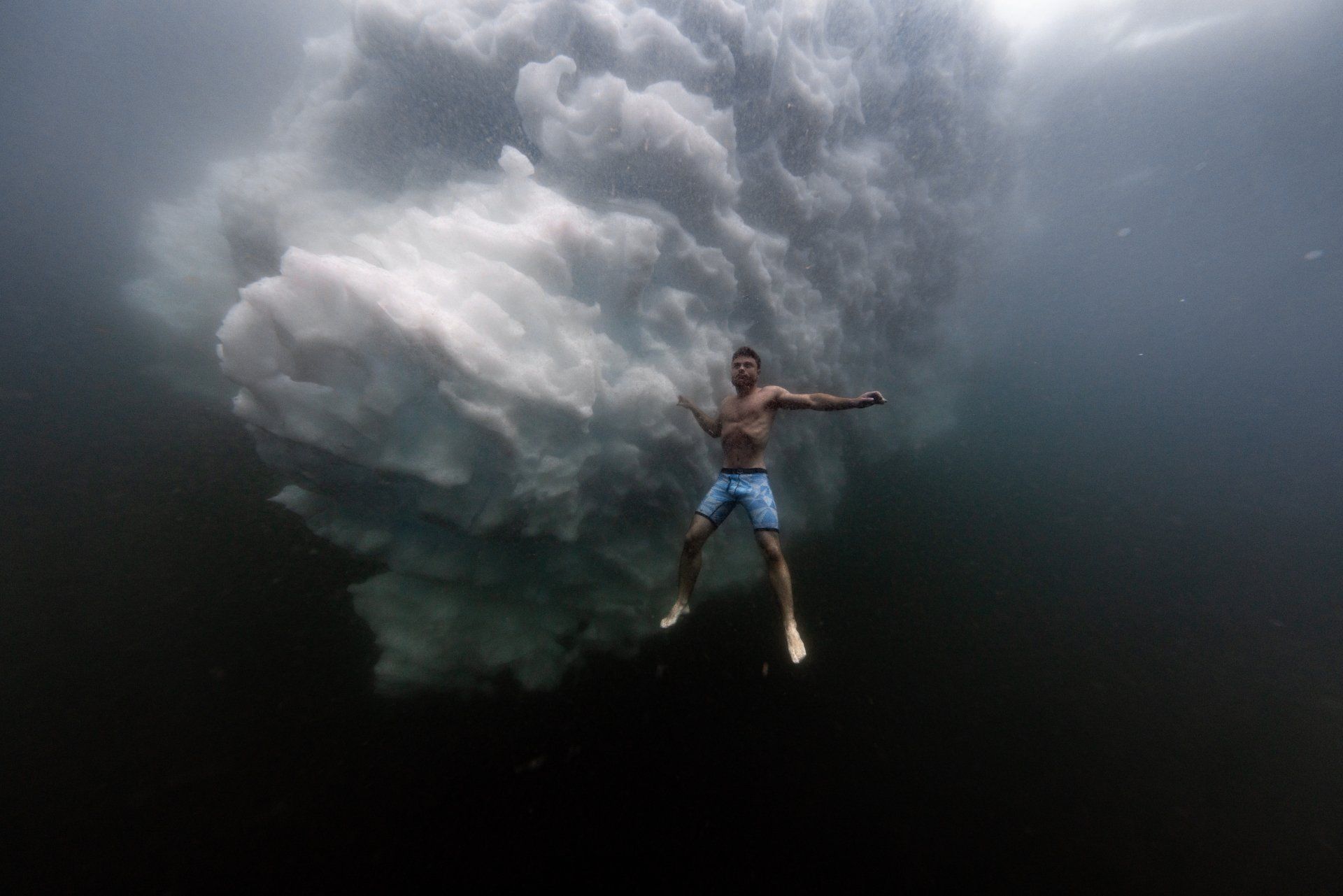 A man is swimming underwater in front of a storm cloud.