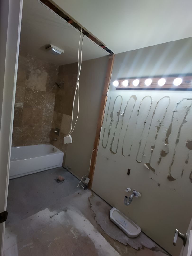 Bathroom under renovation with bathtub, exposed wall, and adhesive on mirror-backed panel