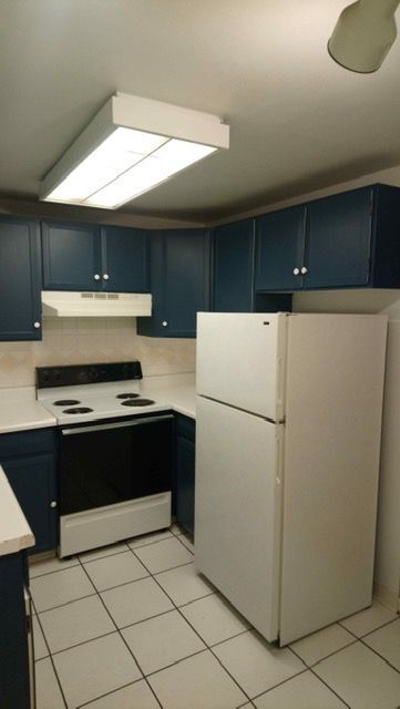 Small kitchen with blue cabinets, white appliances, tiled floor, and a ceiling light