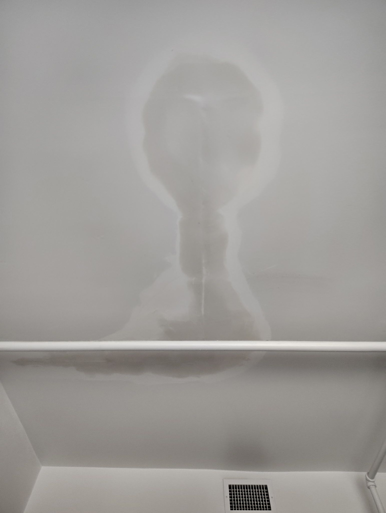 Steam silhouette on a bathroom wall above a vent, with a horizontal ledge in the foreground.
