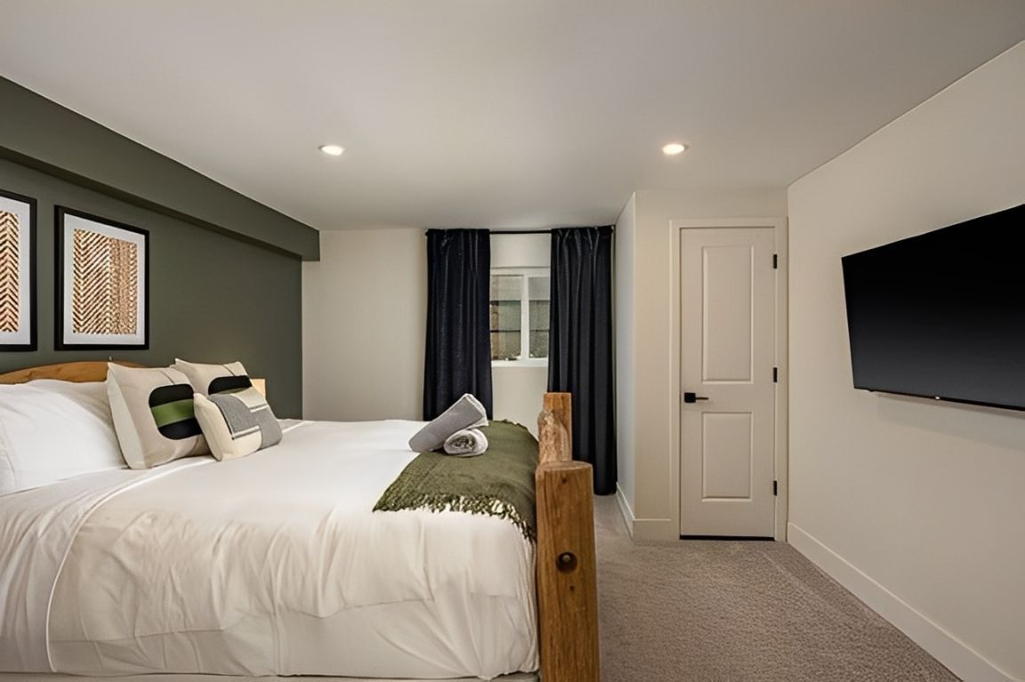 Modern bedroom with a large bed, wall-mounted TV, dark curtains, and neutral decor
