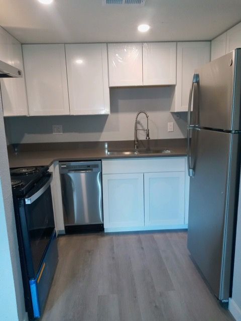 Modern white kitchen with stainless steel appliances, light wood floor, and gray backsplash