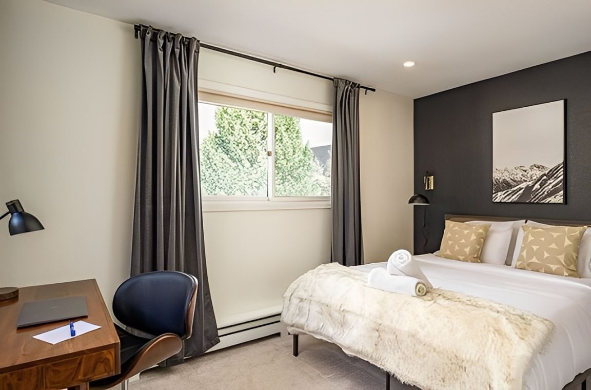 Modern bedroom with bed, desk, dark curtains, and window with trees outside