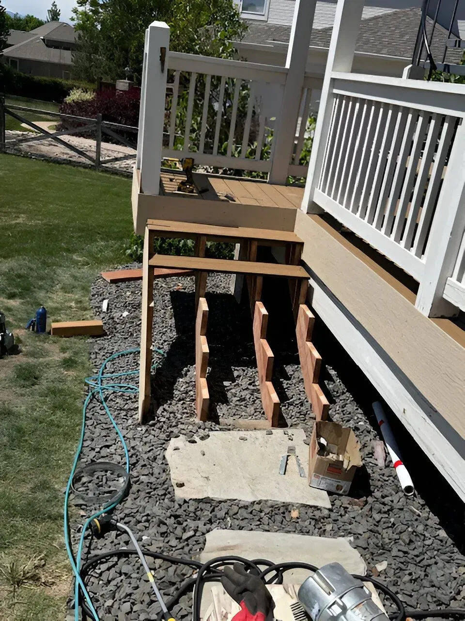 Porch staircase under repair with exposed wooden supports and tools on a gravel path