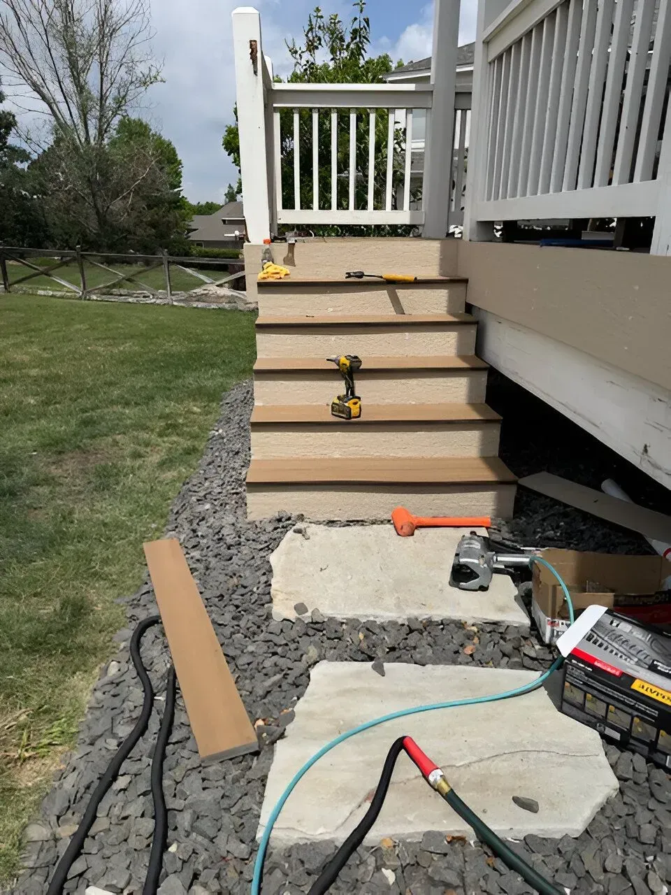 Deck stairs under construction with tools, lumber, and gravel work area