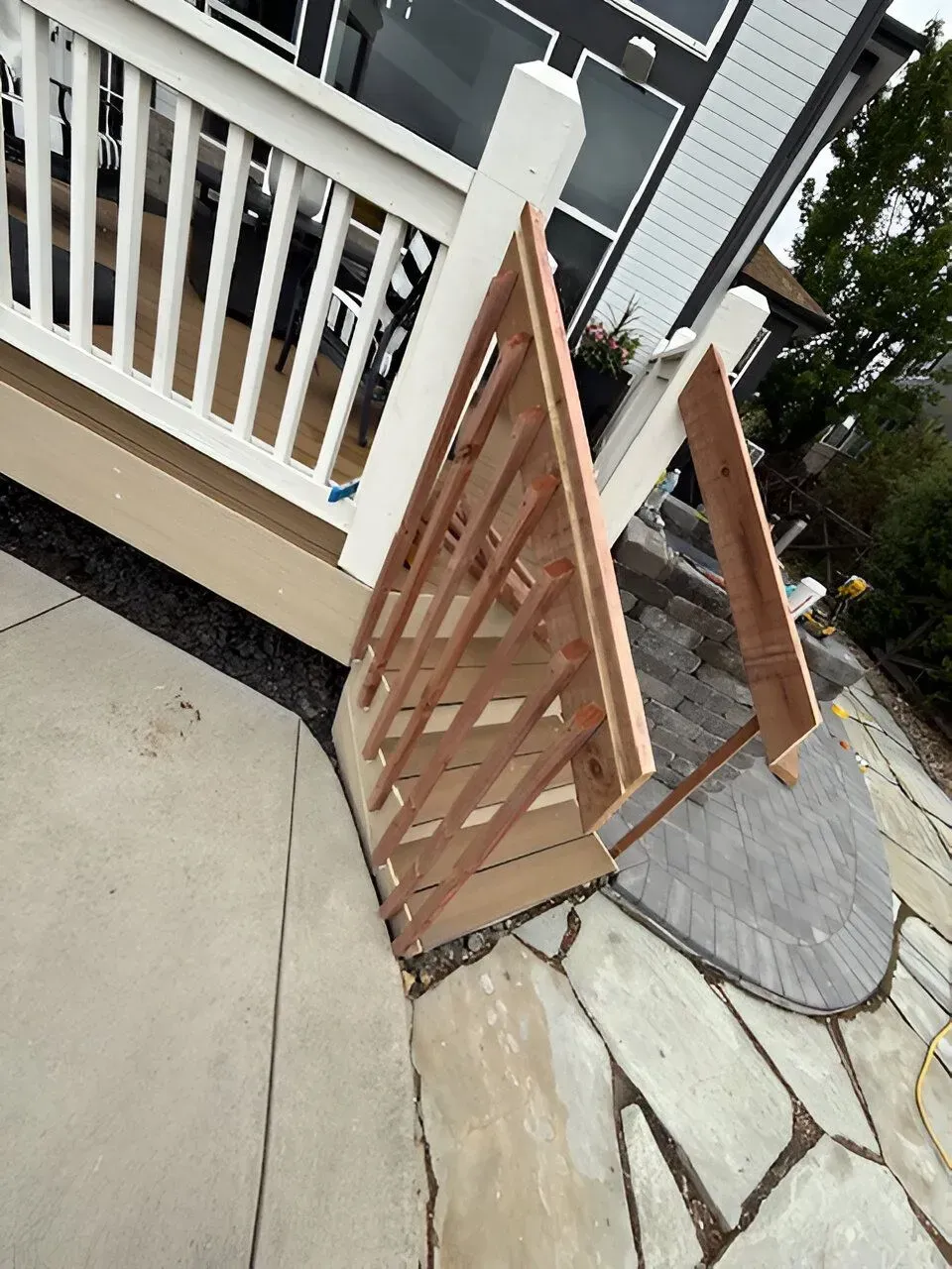 Wooden gate leaning open beside a white porch railing on a stone-and-concrete walkway