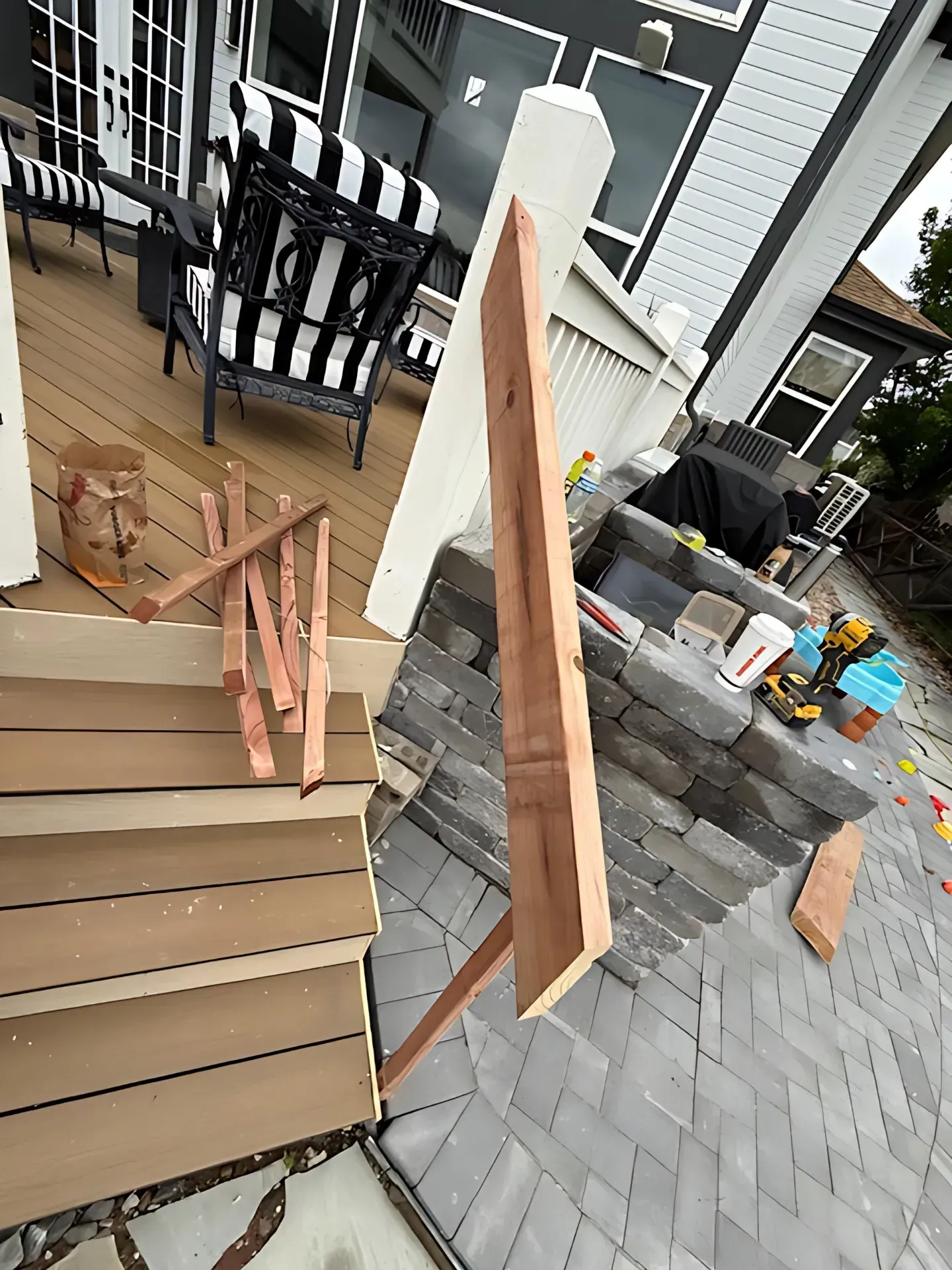 Stack of cardboard panels and a hanging frame on a porch beside a stone planter and rocking chairs.