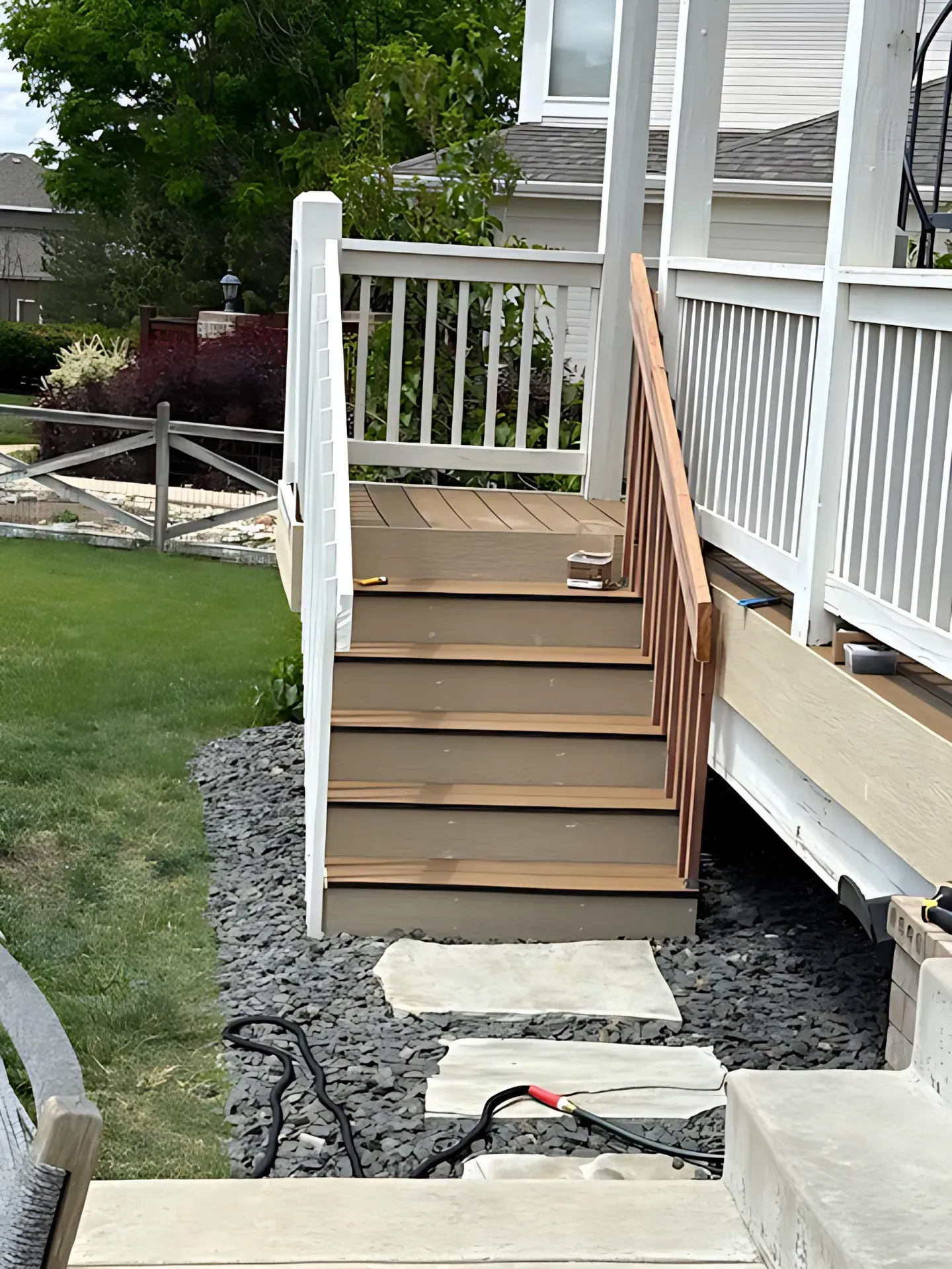 Front porch steps with white railings, brown treads, and a stone walkway in a yard.