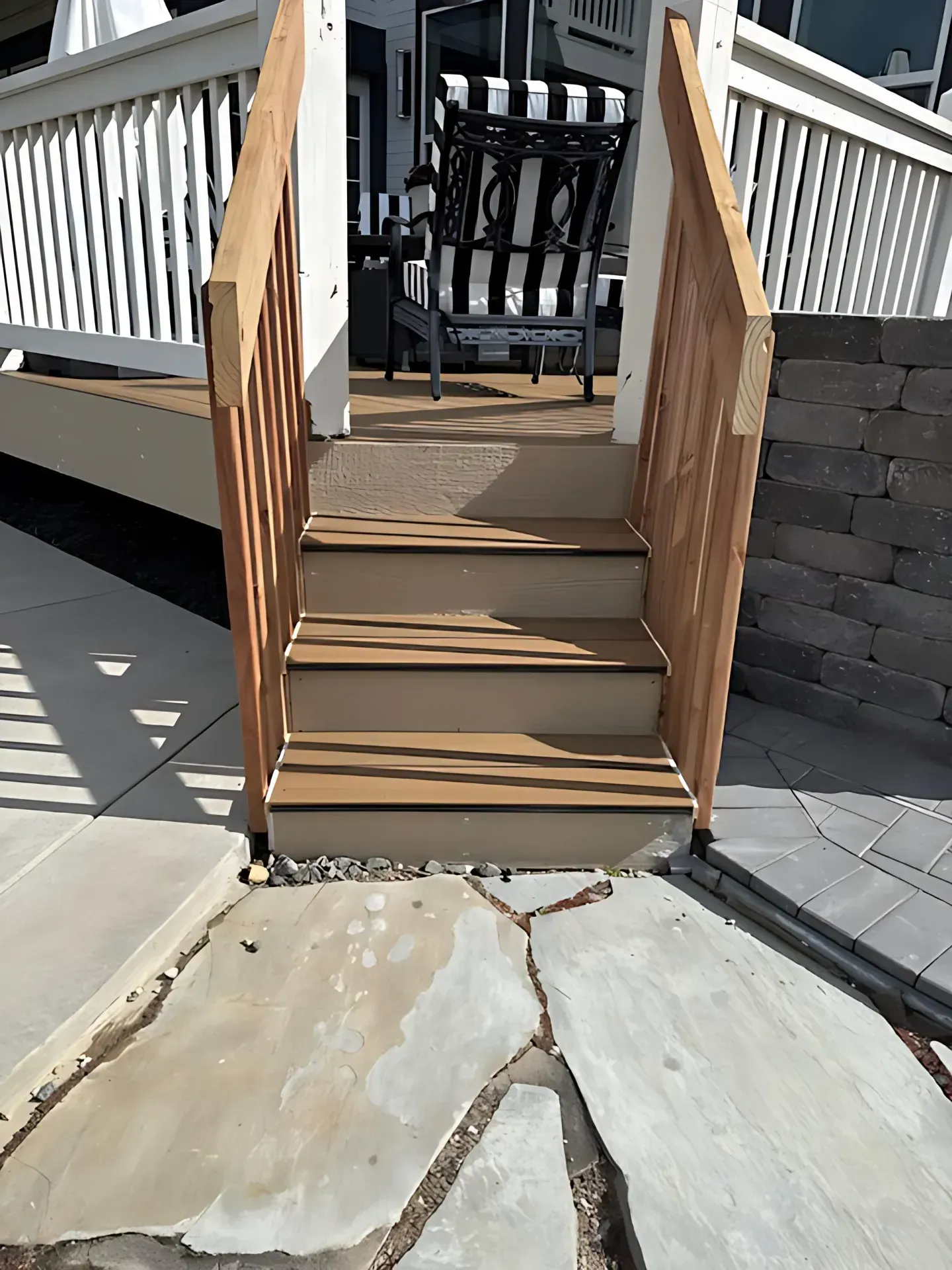 Wooden deck steps with white railings leading to a patio and black outdoor chair.