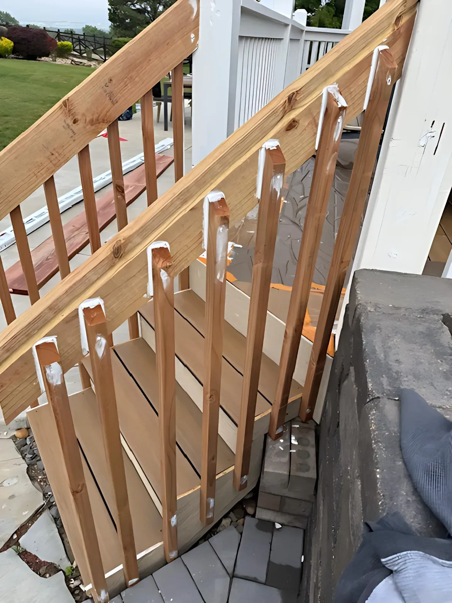 Wooden stair railing with vertical balusters and open deck steps beside a driveway