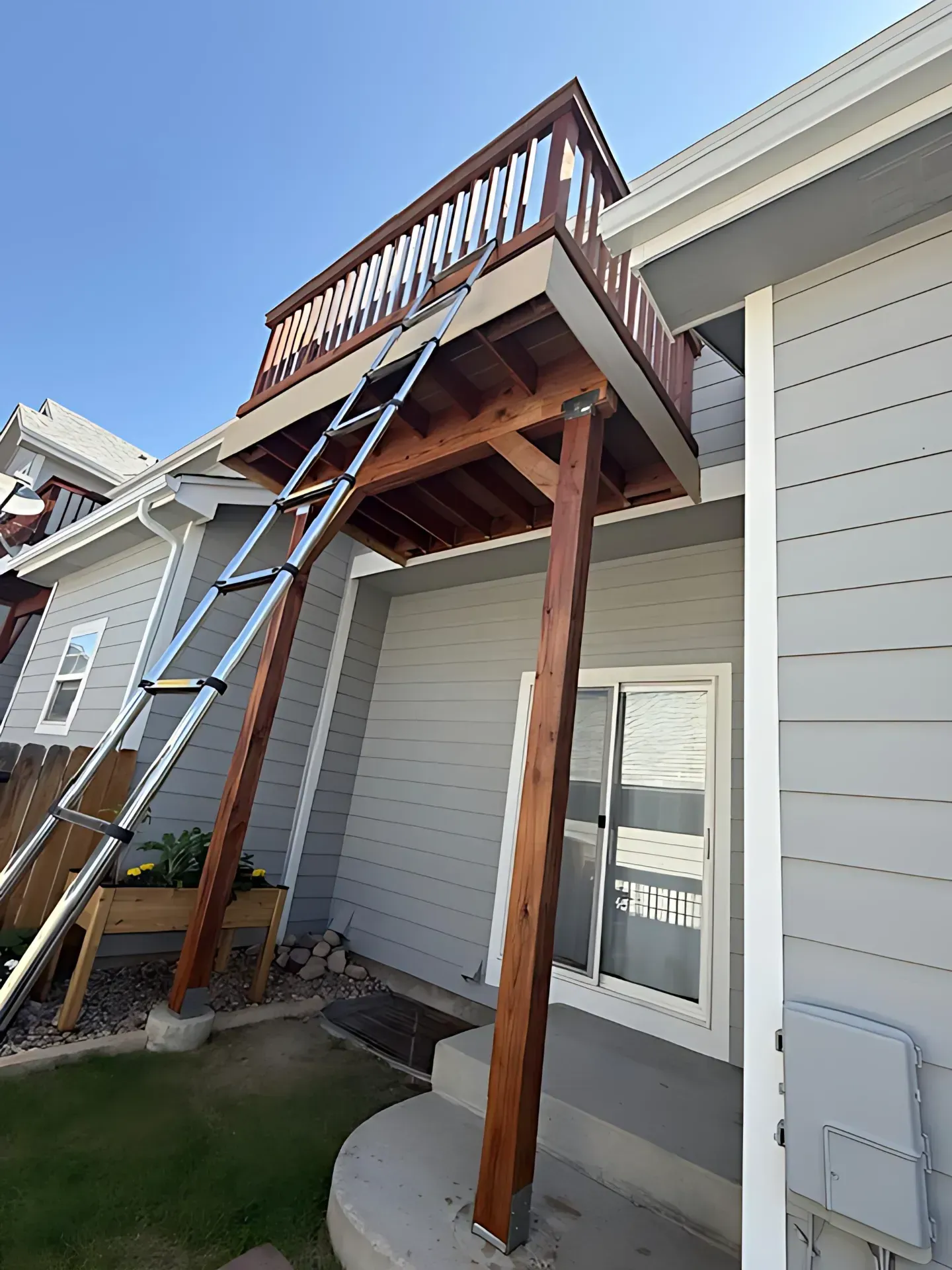 Wooden deck and railing above a home entrance, with a ladder leaning up to it.
