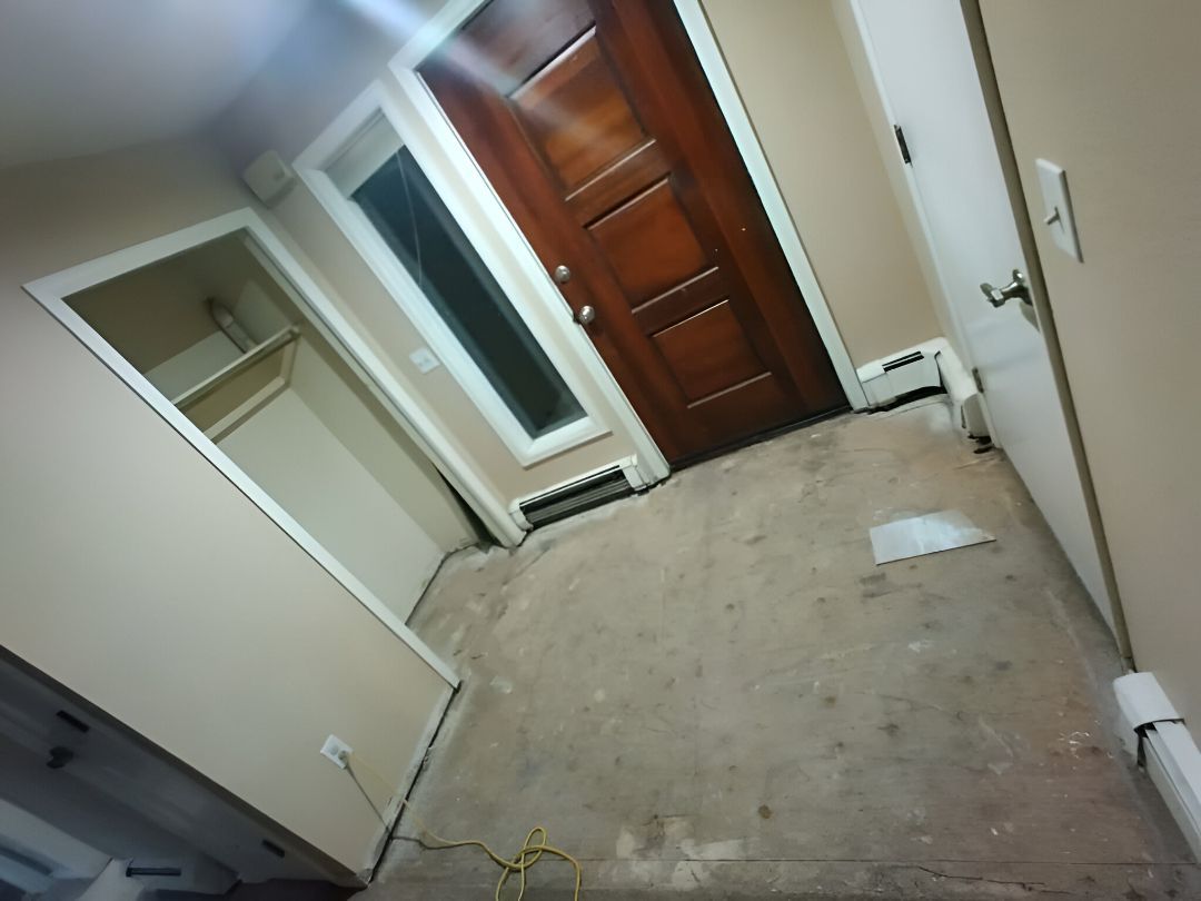 Empty beige bedroom with closet, window, and wooden door, viewed at an angle.