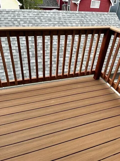 Wooden deck with brown railing overlooking neighboring rooftops and a red house.