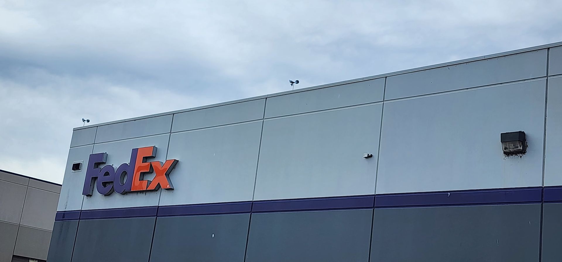 FedEx sign on a light gray warehouse wall with a dark blue stripe