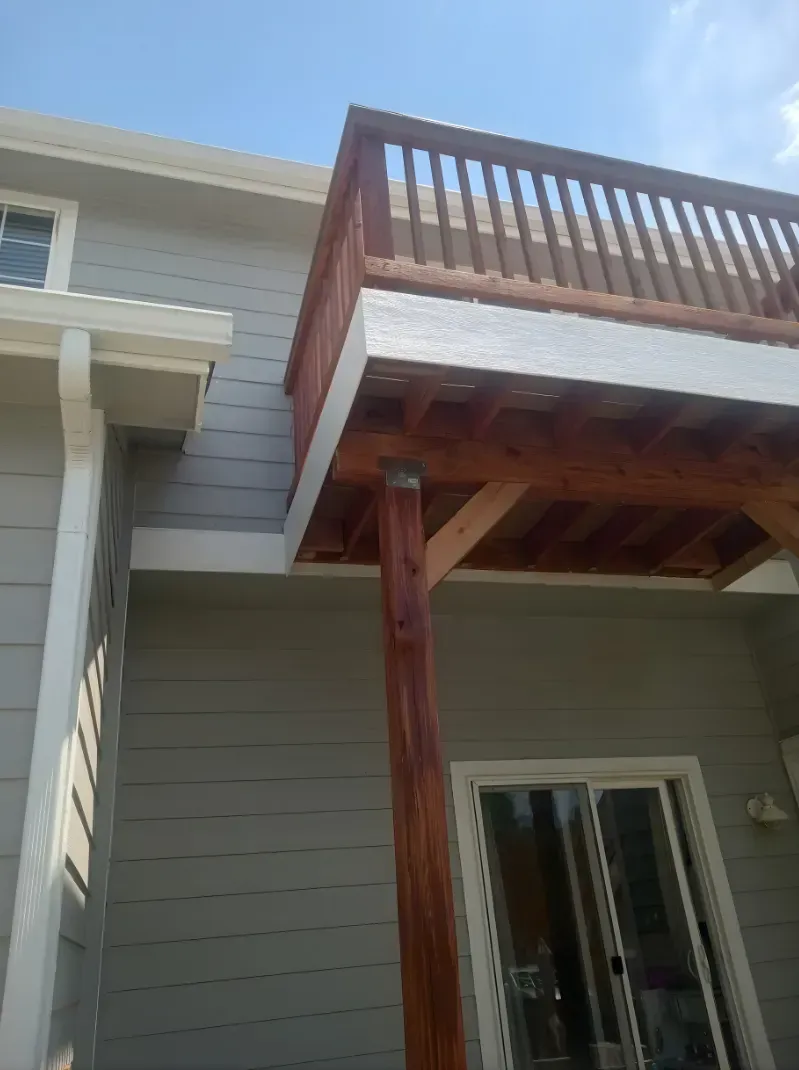 House exterior with an elevated wooden deck and balcony above a sliding glass door.