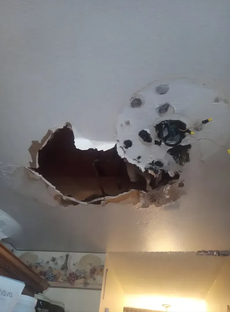 Ceiling with a large hole and exposed material near a round light fixture in a room