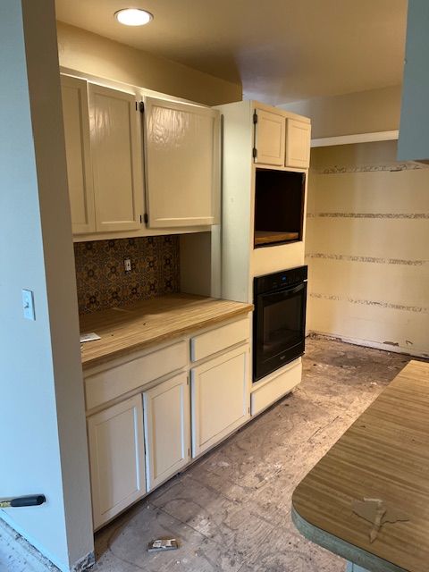 Kitchen with cream cabinets, built-in oven, tiled backsplash, and a partial island in warm lighting