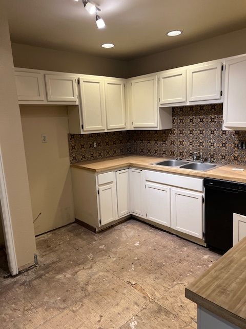 Empty kitchen with white cabinets, brown tile backsplash, and bare floor under ceiling lights.