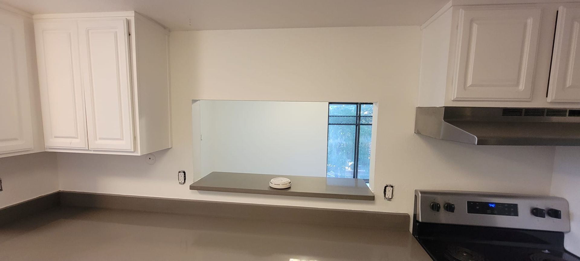 White kitchen with cabinets, gray countertop, pass-through opening, and a stove on the right.