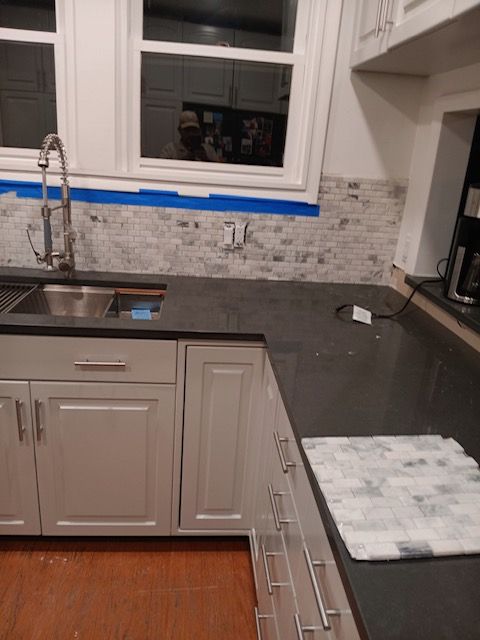 Kitchen with white cabinets, gray countertops, tiled backsplash, and a window above the sink under renovation.