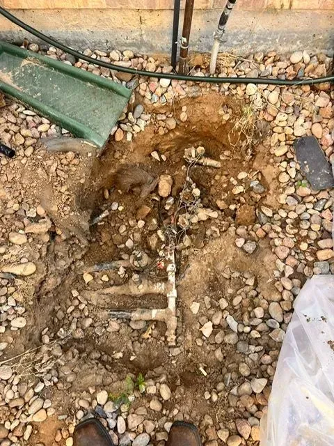 Mud-filled trench in rocky ground beside a green pipe and hose, with a plastic sheet at the edge.