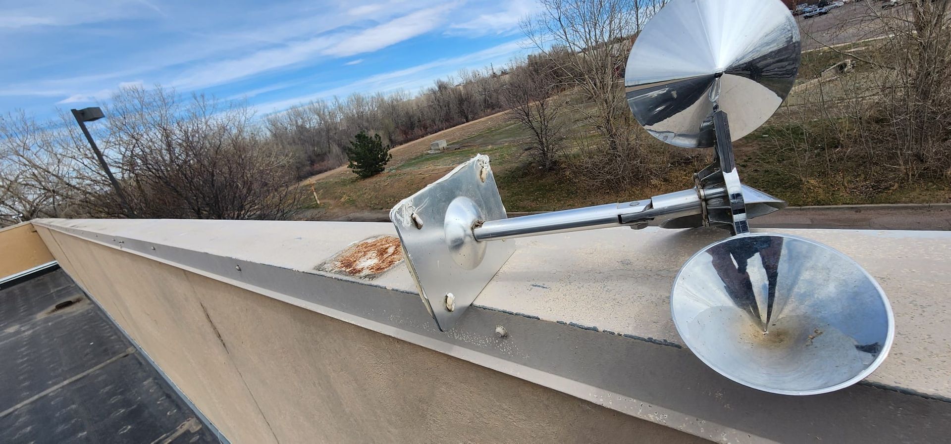 Small rooftop weather instrument with shiny metal discs under a blue sky on a concrete ledge