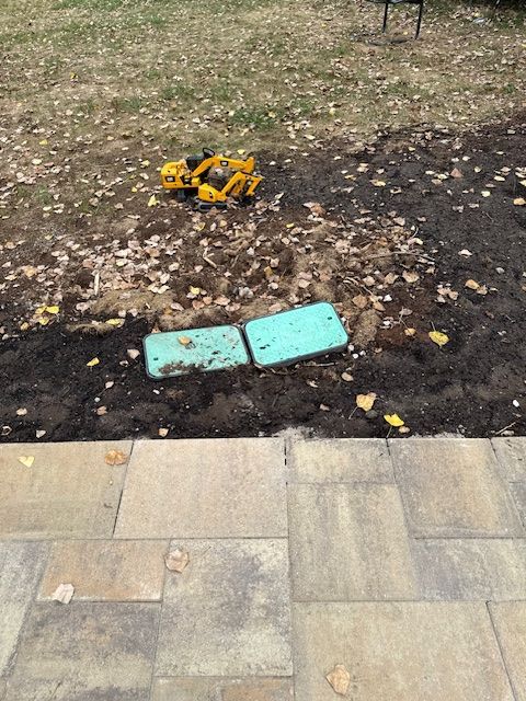 Yellow construction equipment beside two turquoise pavers on a dirt area next to a paved walkway