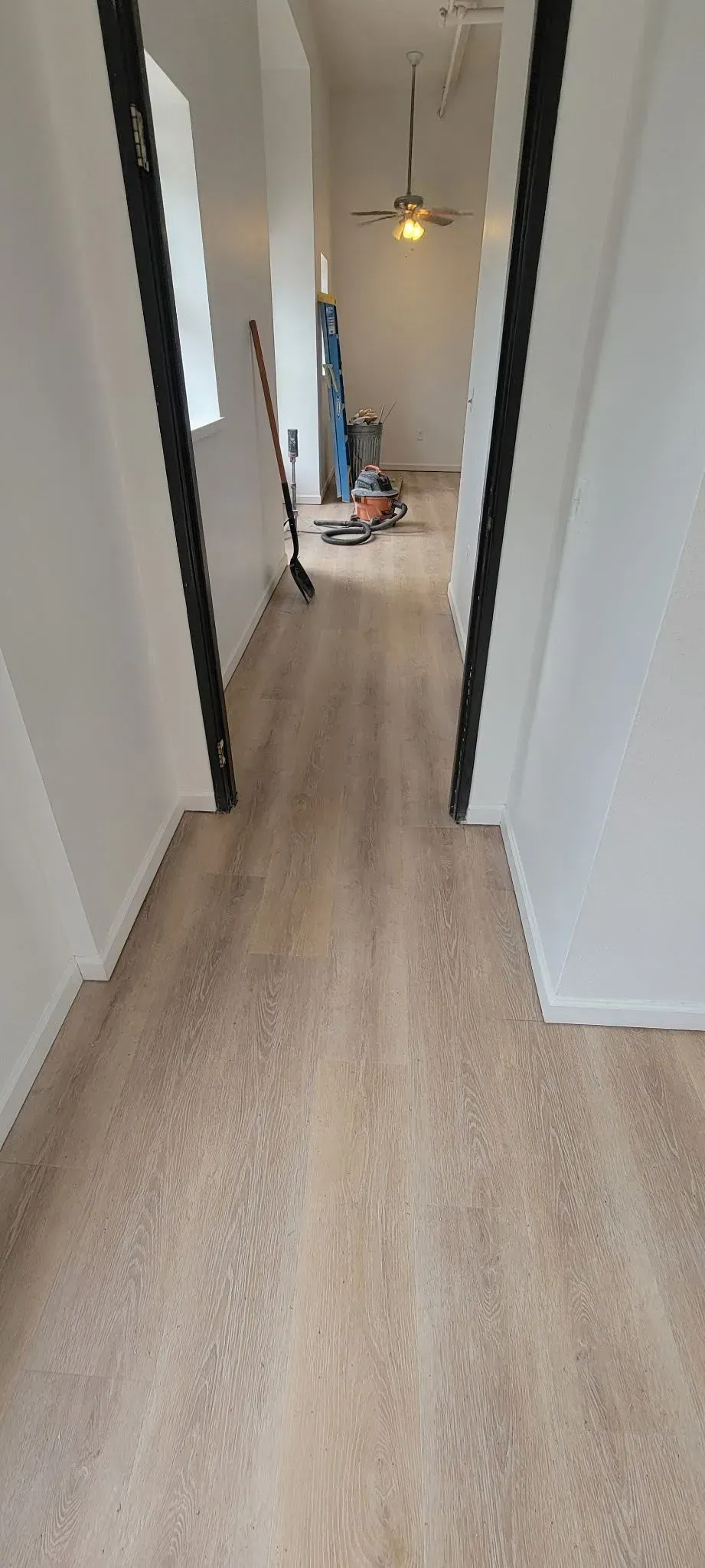 Narrow hallway with light wood floors, white walls, and a room visible at the end.