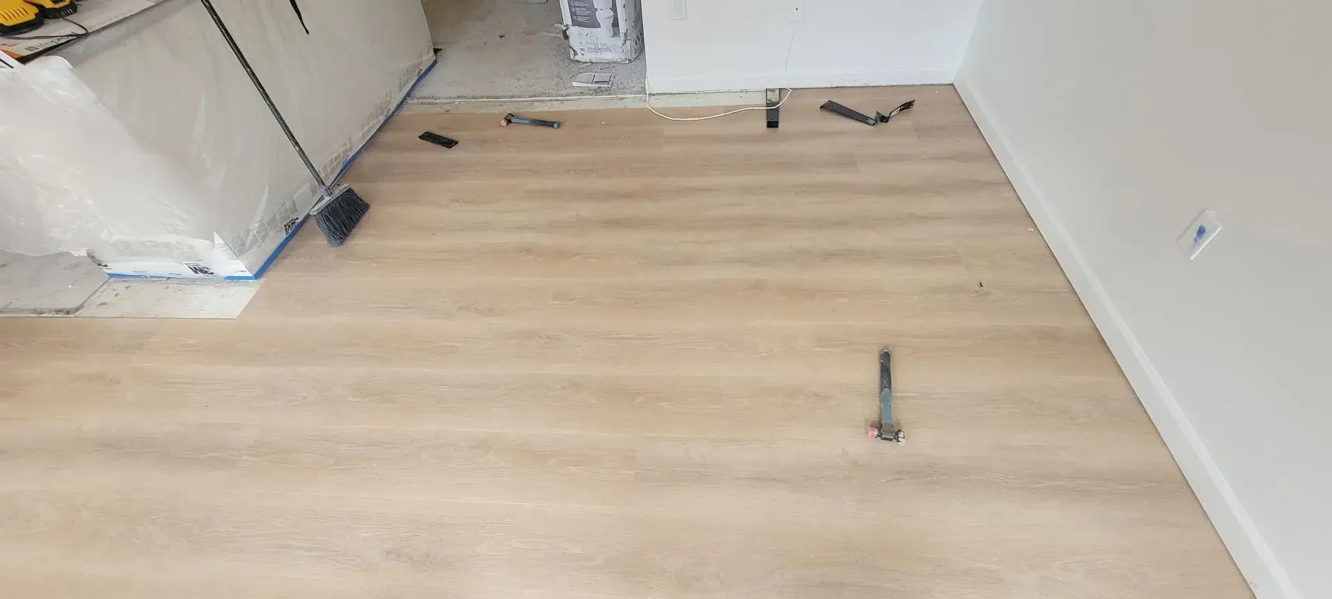 Empty room with light wood flooring, white walls, and scattered construction tools and materials