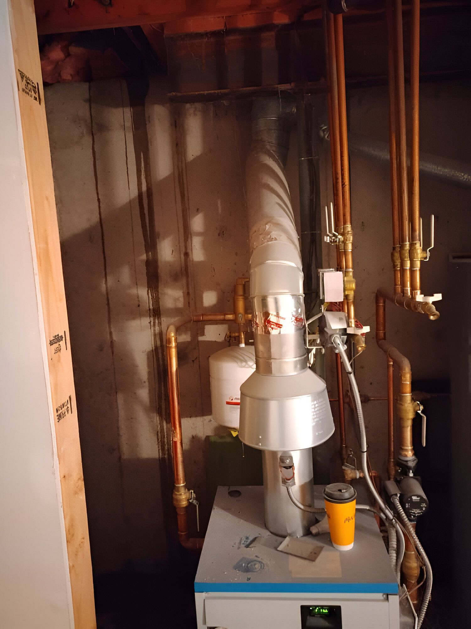 Gas furnace and ductwork in a dim utility closet, with exposed copper pipes and a yellow filter on top.