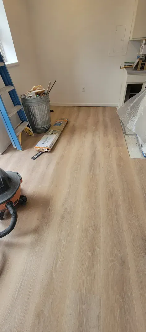 Renovation room with light wood flooring, a blue ladder, and tools on the floor near a white wall.