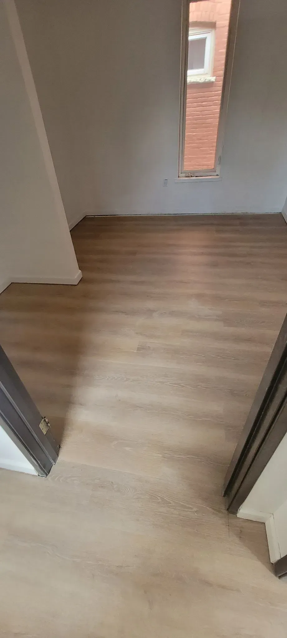 Empty hallway with light wood flooring and a narrow window at the end.