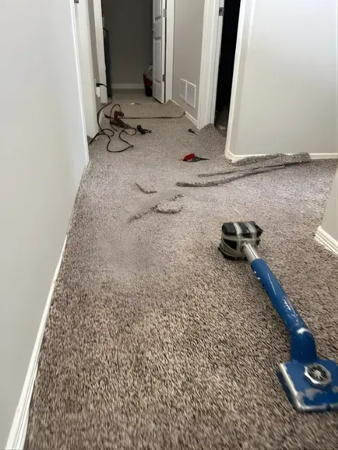 Carpet-cleaning wand on beige carpet in a hallway with scattered cords and debris