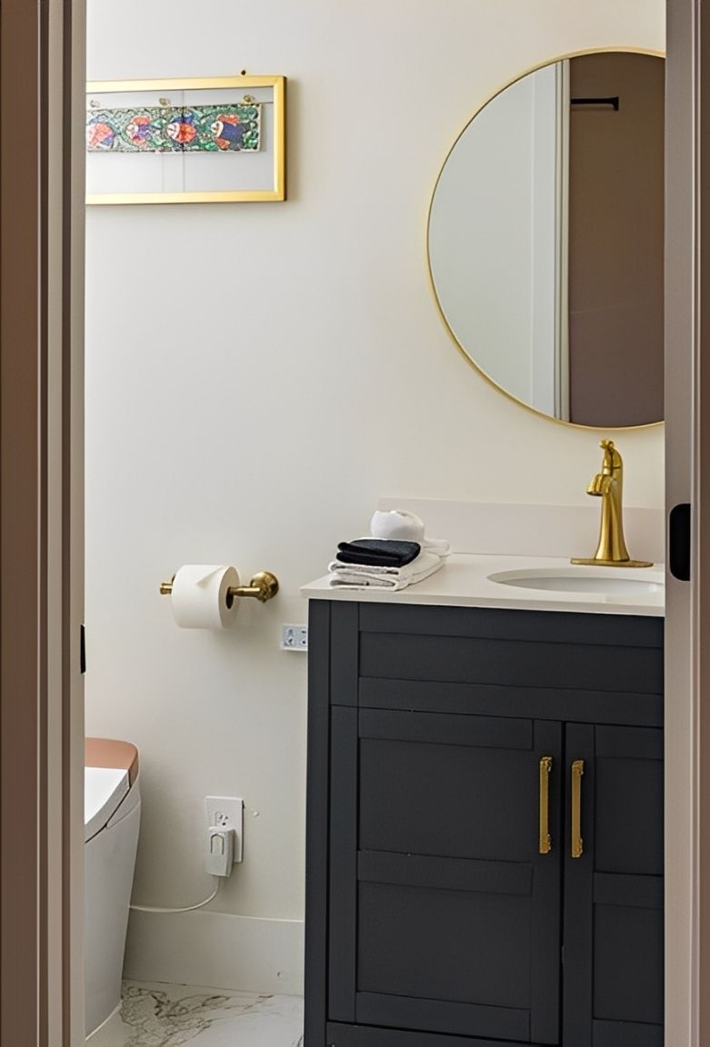 Small bathroom vanity with dark cabinets, gold faucet, round mirror, and wall art.