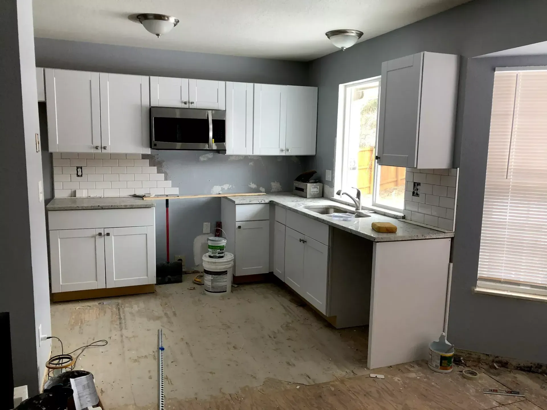 Partially renovated kitchen with white cabinets, gray walls, and exposed floor under construction