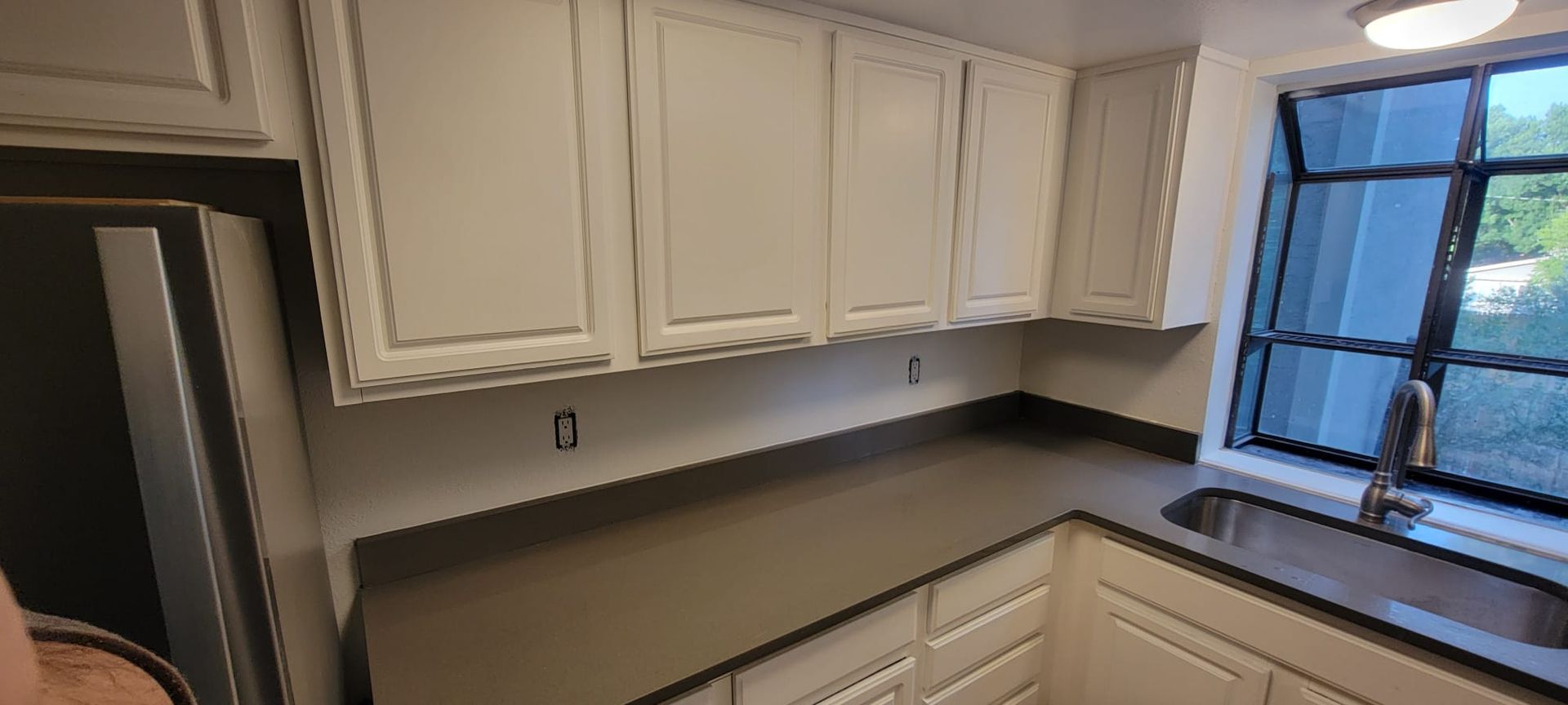Small kitchen with white cabinets, gray countertops, and a window over the sink.
