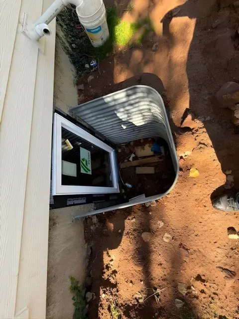 Open utility box in the ground beside a house, with tools inside and dirt around it
