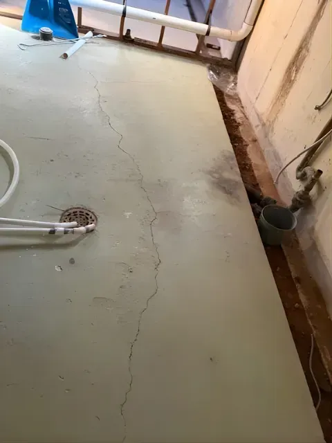 Bathroom floor with a long crack, drain, and pipe along the wall