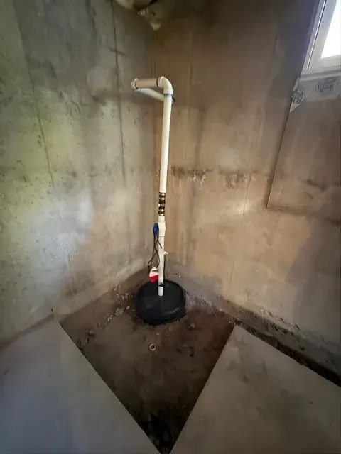 Small basement sump pump with white pipe in a concrete utility pit