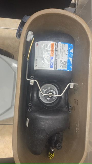 Open tank-style toilet with exposed black internal mechanism and blue label inside beige seat.