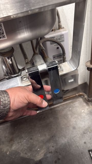 Hand holding a black-and-silver device near a stainless steel sink in a kitchen or utility area