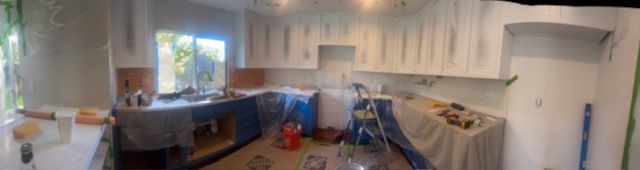 Messy kitchen under renovation with cabinets, tools, and covered countertops